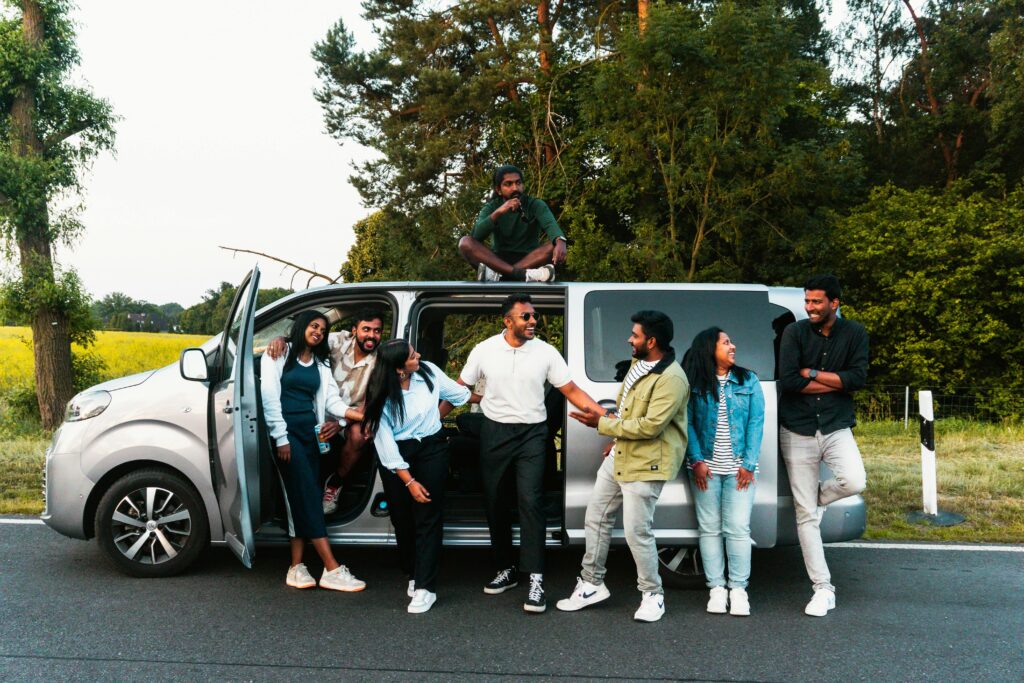 A group of friends having fun by a van on a scenic road trip in nature.